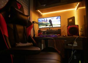 A gaming setup featuring a ThunderX3 gaming chair, a desktop computer with a widescreen monitor, and LED backlighting.